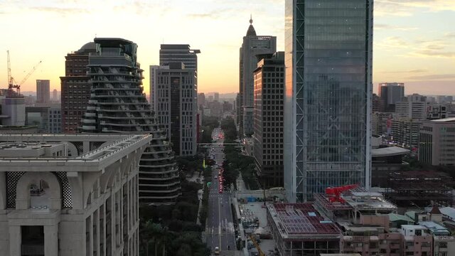 Cinematic aerial dolly in shot, drone flying above Songgao road with high-rise skyscrapers and apartment complex alongside at sunset in downtown Xinyi district, Taipei city, Taiwan.
