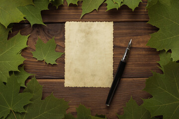 A sheet of antique paper and a fountain pen in a frame of maple leaves on a wooden background....