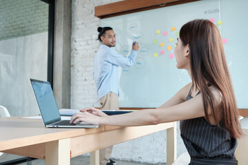 Obraz premium Two colleagues and coworkers of Asian ethnicity brainstorm and meeting finance project discuss with business plan in conference room with colorful sticky notes paper on writing board in the office.