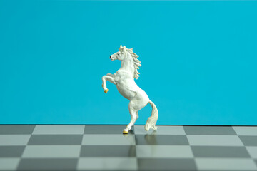 Miniature of white prancing horse standing on chessboard isolated on blue background.