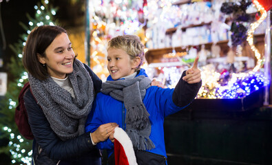 Happy tween boy choosing Xmas decorations and gifts on street fair with his loving mother..