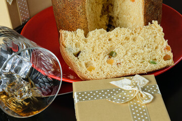 Closeup of a slice of panettone next to an overturned whiskey glass and a gift box.