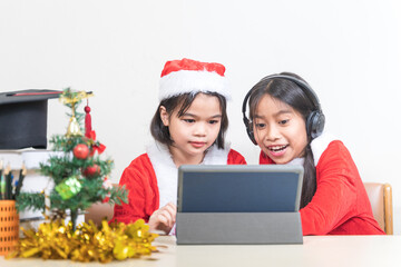 Two Asian children little girls wear Christmas Santa Claus chating with friend on digital tablet. Christmas Holiday Concept Stock Photo