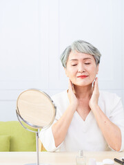 Senior Asia woman is spraying perfume at home.