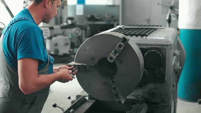 The turner performs maintenance and repair of the lathe in the workshop. Slow motion video. Medium shot. A man of 50 years in a work jumpsuit stands behind the workplace in production.