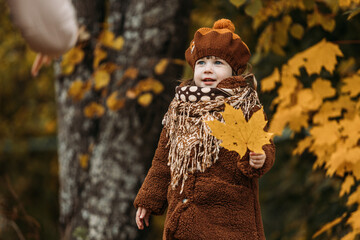 A dreamy little girl in a brown beret and autumn clothes on an autumn background. A smiling child is playing in the autumn park.