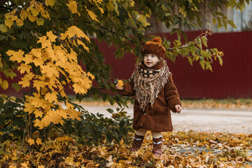 A dreamy little girl in a brown beret and autumn clothes on an autumn background. A smiling child is playing in the autumn park.