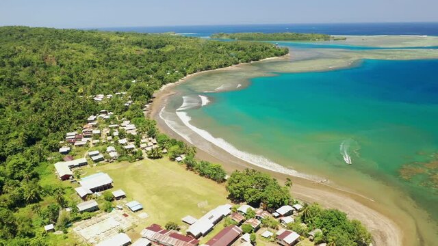 Aerial view of an outboard boat arriving near the shore of a seaside village.