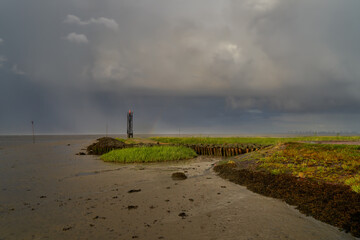 dark cloudy sky with a pale rainbow over the lighthouse and the mud flats of the Wadden Sea in Fedderwardersiel (district Wesermarsch, Germany)