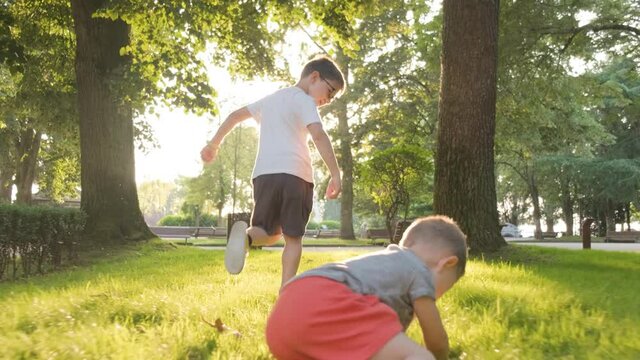 Two Young Boys Running in a Park and One Boy Stumbles on the Ground, Gimbal Follow Shot, Running Away From Camera