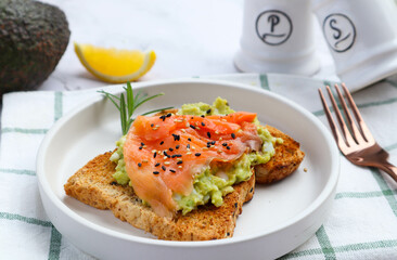Toast with avocado and smoked salmon sprinkled on top with sesame seed at close up view - healthy eating concept