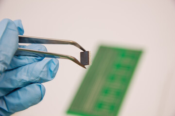 Hand in blue glove holds tweezers with smd compenent chip for pcb