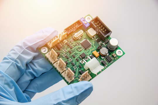 Hand in a blue glove holds pcb chip assembly on pcb backround on the production of printed circuit boards