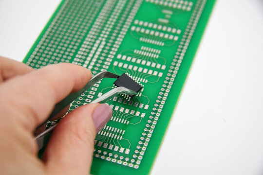 Hand holds tweezers with smd compenent chip for pcb