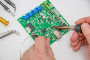 Male hands solder components onto a printed circuit board using copper and a soldering iron....