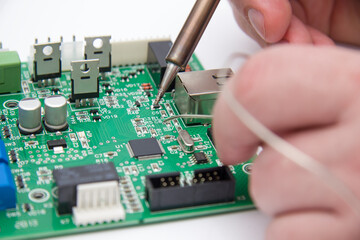 Fototapeta premium Male hands solder components onto a printed circuit board using copper and a soldering iron. Electronics repair. Selective focus.