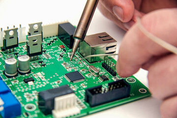 Male hands solder components onto a printed circuit board using copper and a soldering iron....