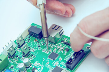 Male hands solder components onto a printed circuit board using copper and a soldering iron. Electronics repair. Selective focus. - obrazy, fototapety, plakaty