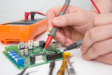 Male measures voltage with an ammeter on a printed circuit board. Electronics repair with tester. Selective focus.