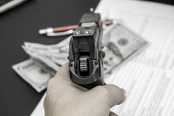 Pistol in the hand, money and documents on the office desk. The concept of blackmail, threats, murder for enrichment