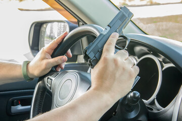 Fototapeta premium Man driving a car with a weapon, gun in his hand. The criminal steals the car. Danger district of the city