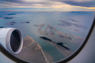 Fototapeta premium View from the window of a passenger plane during the climb over the Yellow Sea. The powerful jet engine - Smaller islands and sandbanks are visible due to the low tide - aerial view 