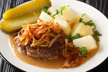 Danish Burgers Hakkebof with Caramelized Onions boiled potatoes and brown gravy close up in the plate on the table. Horizontal