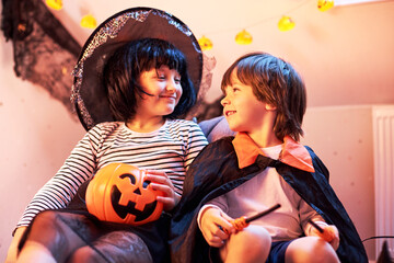 Cheerful boys and a girl in suits eat sweets from pumpkin buckets