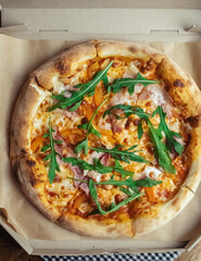 Close-up of pizza with bacon in a disposable dish. Top view of takeaway food in a fast food cafe. On photo - mozzarella cheese, tomatoes, and red basil. Classic recipe