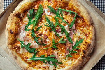 Close-up of pizza with bacon in a disposable dish. Top view of takeaway food in a fast food cafe. On photo - mozzarella cheese, tomatoes, and red basil. Classic recipe