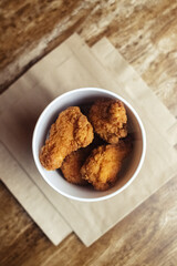 Close-up of chicken wings fried in batter. In a fast food restaurant, there is a cardboard box of chicken and sauce on the table. Sun rays fall beautifully on the hand of the girl who holds the food