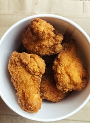 Close-up of chicken wings fried in batter. In a fast food restaurant, there is a cardboard box of chicken and sauce on the table. Sun rays fall beautifully on the hand of the girl who holds the food