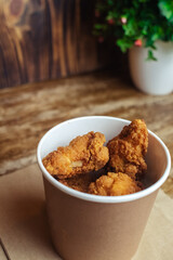 Close-up of chicken wings fried in batter. In a fast food restaurant, there is a cardboard box of chicken and sauce on the table. Sun rays fall beautifully on the hand of the girl who holds the food