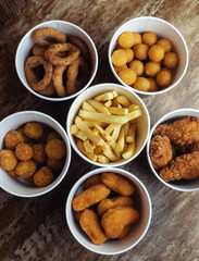 Top view of onion rings, cheese balls, chicken nuggets, wings in batter, fries and cheese sticks. Six-course set in paper buckets. Fast food cafes and restaurants. Food is laid out in shape of flower