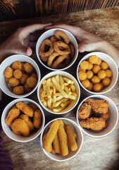 Top view of onion rings, cheese balls, chicken nuggets, wings in batter, fries and cheese sticks. Six-course set in paper buckets. Fast food cafes and restaurants. Food is laid out in shape of flower