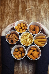 Top view of onion rings, cheese balls, chicken nuggets, wings in batter, fries and cheese sticks. Six-course set in paper buckets. Fast food cafes and restaurants. Food is laid out in shape of flower