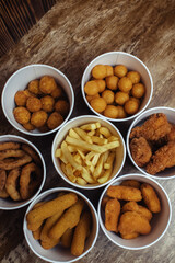 Top view of onion rings, cheese balls, chicken nuggets, wings in batter, fries and cheese sticks. Six-course set in paper buckets. Fast food cafes and restaurants. Food is laid out in shape of flower