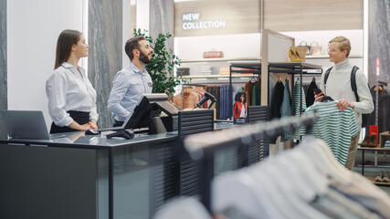 Clothing Store: Handsome Young Man At Checkout Counter Buys Clothes from Friendly Retail Sales...