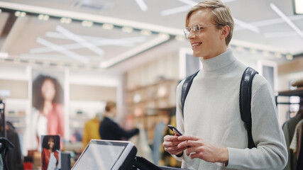 Clothing Store: Portrait of a Young Man At Checkout Counter Buying Clothes, Ready to Pay with...