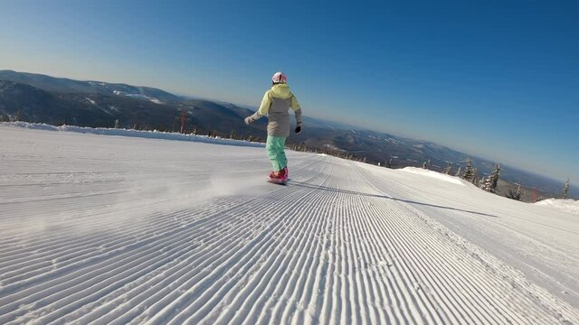SLOW MOTION: a girl on a snowboard rides in the morning on fresh corduroy on a ski track. second-person view, camera pursuit. the concept of active recreation in winter. 2k prores
