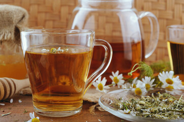 Glass of chamomile tea with honey and flowers on wooden table