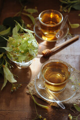 Hot herbal tea with linden flowers and honey on wooden background in sunshine