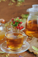 Teapot and cups of herbal tea with herbal flowers and strawberries on wooden table