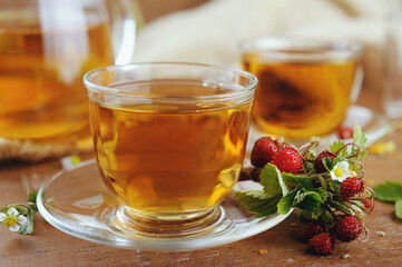 Teapot and cups of herbal tea with herbal flowers and strawberries on wooden table