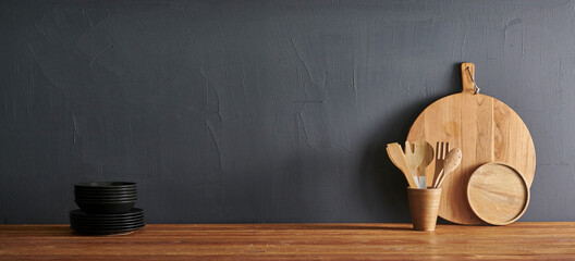 Wooden table, kitchen utensil, wooden cutting board, fork, knife, spoon and stone wall background.