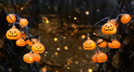 jack-o' lantern garlands and lights bokeh in dark mysterious forest. symbol of Halloween holiday, Samhain sabbat. festive autumn season. copy space - obrazy, fototapety, plakaty