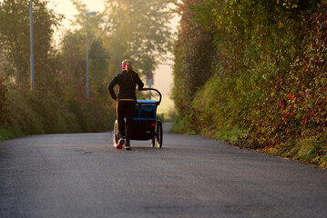 Woman with baby buggy jogging on rural road on a beautiful foggy autumn morning. Photo taken October 16th, 2021, Zurich, Switzerland.