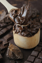Chocolat butter in wooden bowl and dark chocolate chips, bar and chopped on brown background