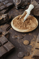 Bars, chopped and chips of  dark chocolate with cacao powder in wooden bowl