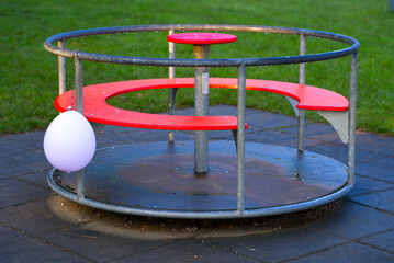 Empty wet red roundabout carousel with pink balloon at playground on a beautiful autumn morning. Photo taken October 16th, 2021, Zurich, Switzerland. 